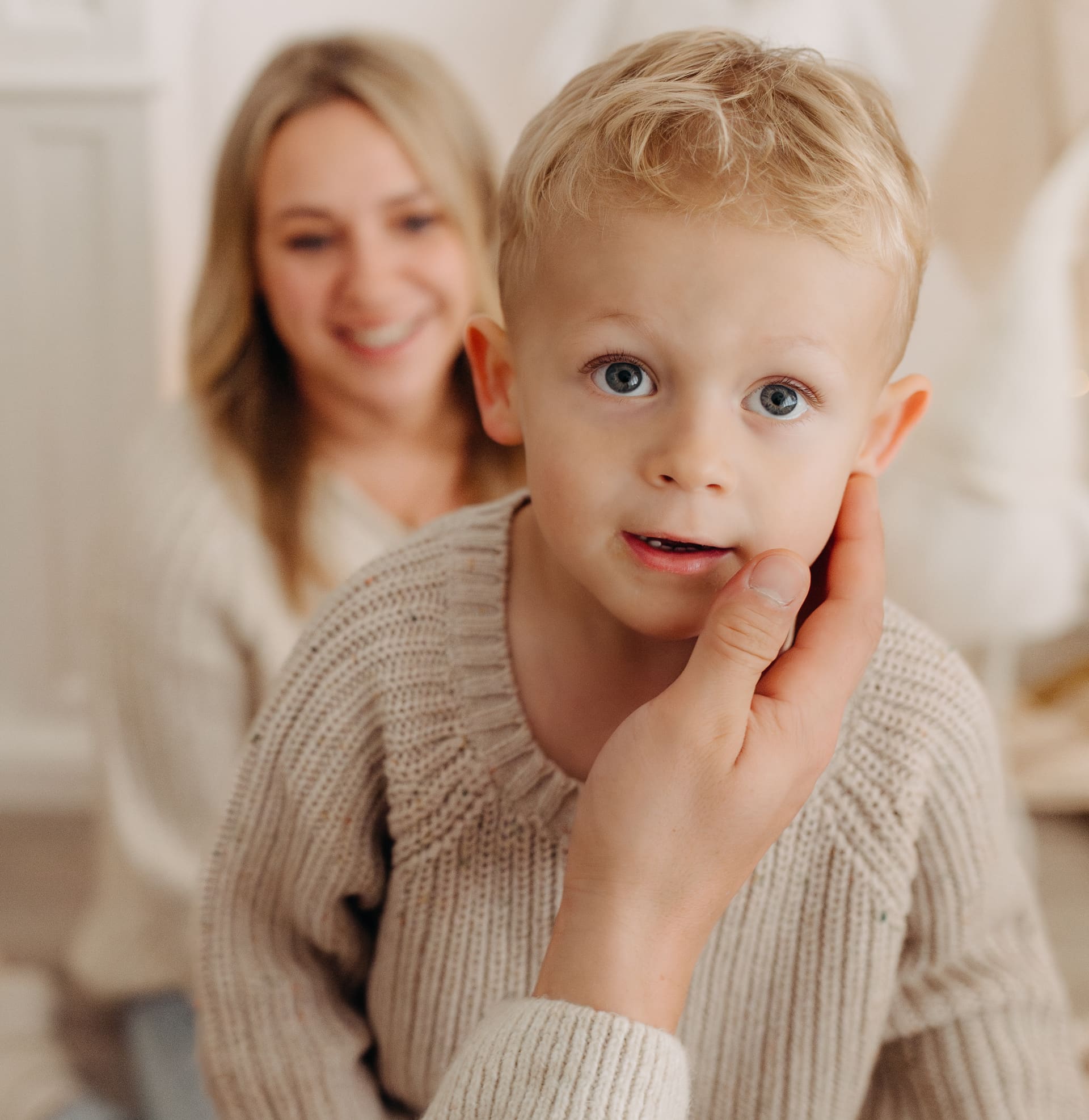 Blonder Junge schaut neugierig in die Kamera, Mama lächelt im Hintergrund — Familien-Shooting Bottrop