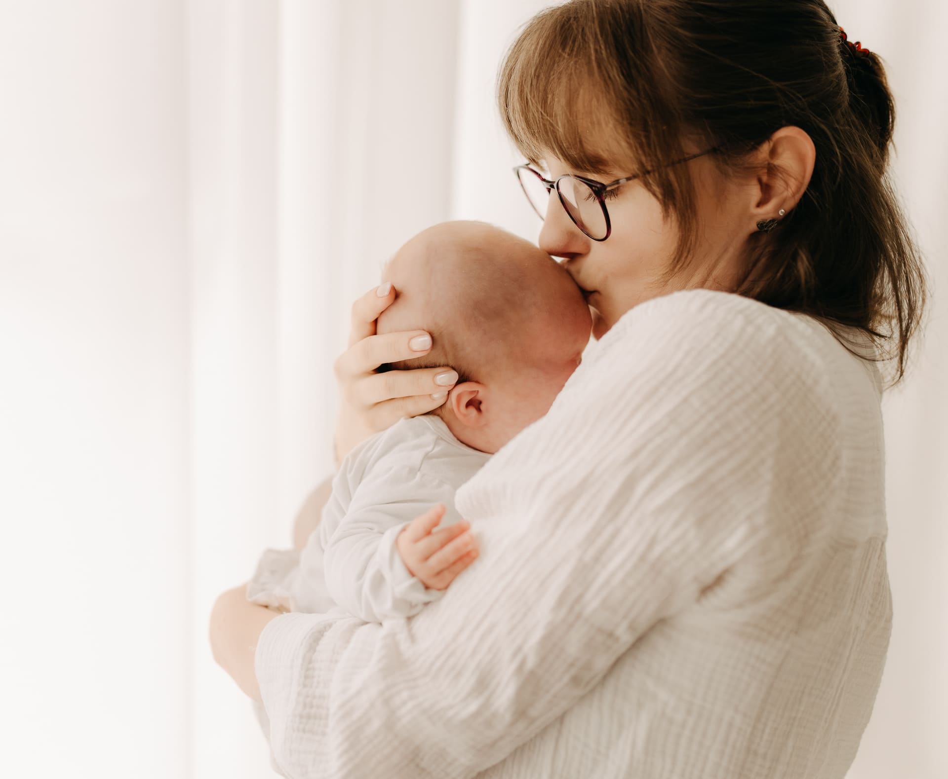 Mama küsst zärtlich ihren Neugeborenen auf den Kopf — Newborn-Shooting im Tageslichtstudio Bottrop
