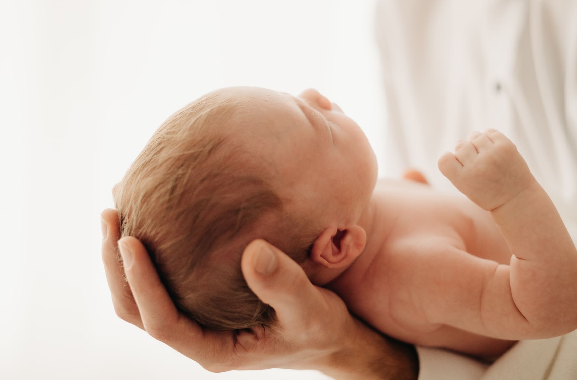 Baby liegt sicher in Papas Händen und ballt das Fäustchen — Newborn-Shooting Bottrop
