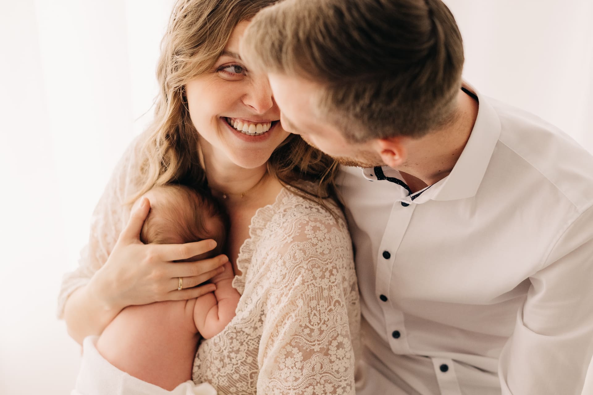 Mama und Papa lachen gemeinsam mit ihrem Neugeborenen — Newborn-Shooting Bottrop