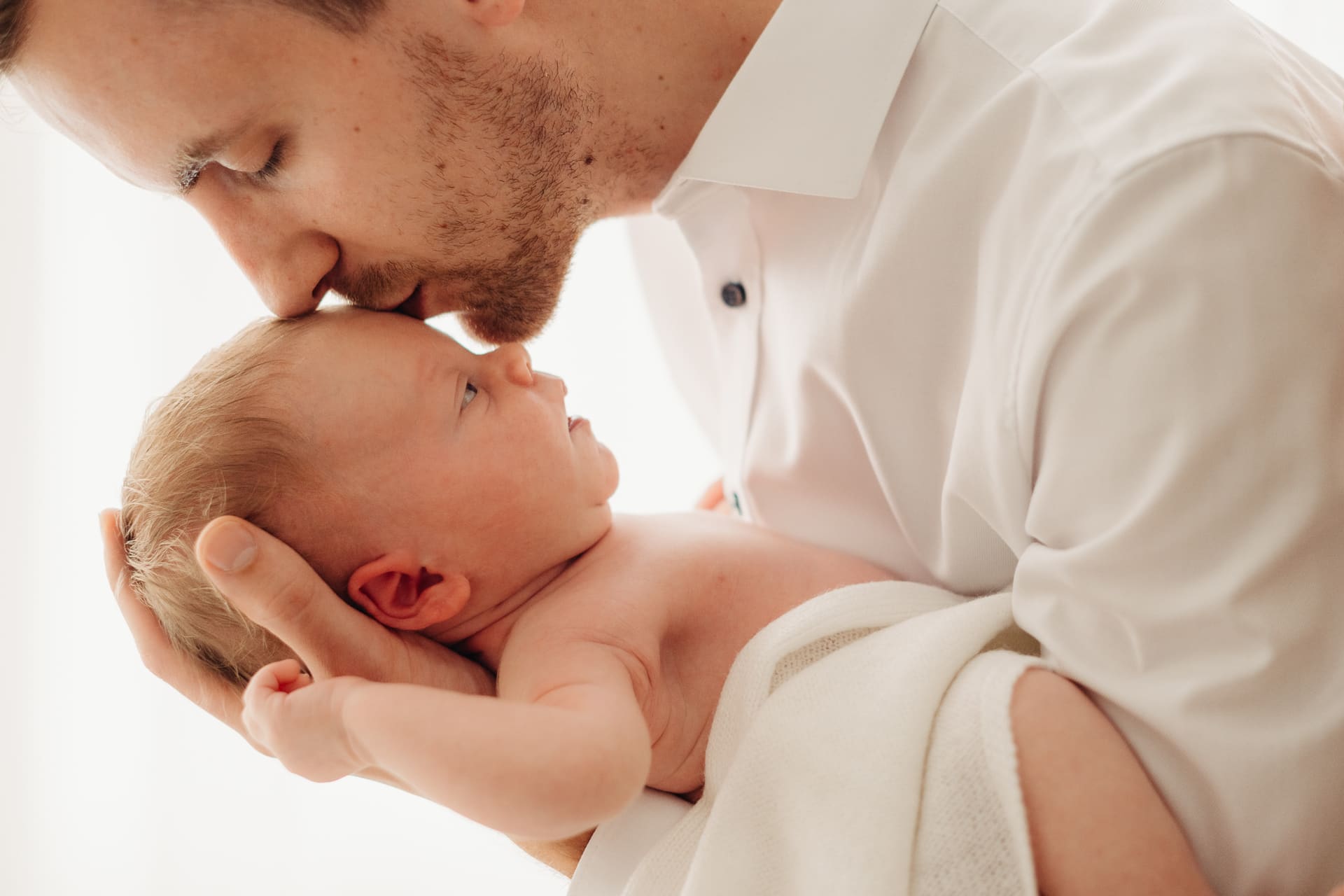 Papa küsst zärtlich sein Neugeborenes auf die Stirn — Newborn-Shooting im Tageslichtstudio Bottrop