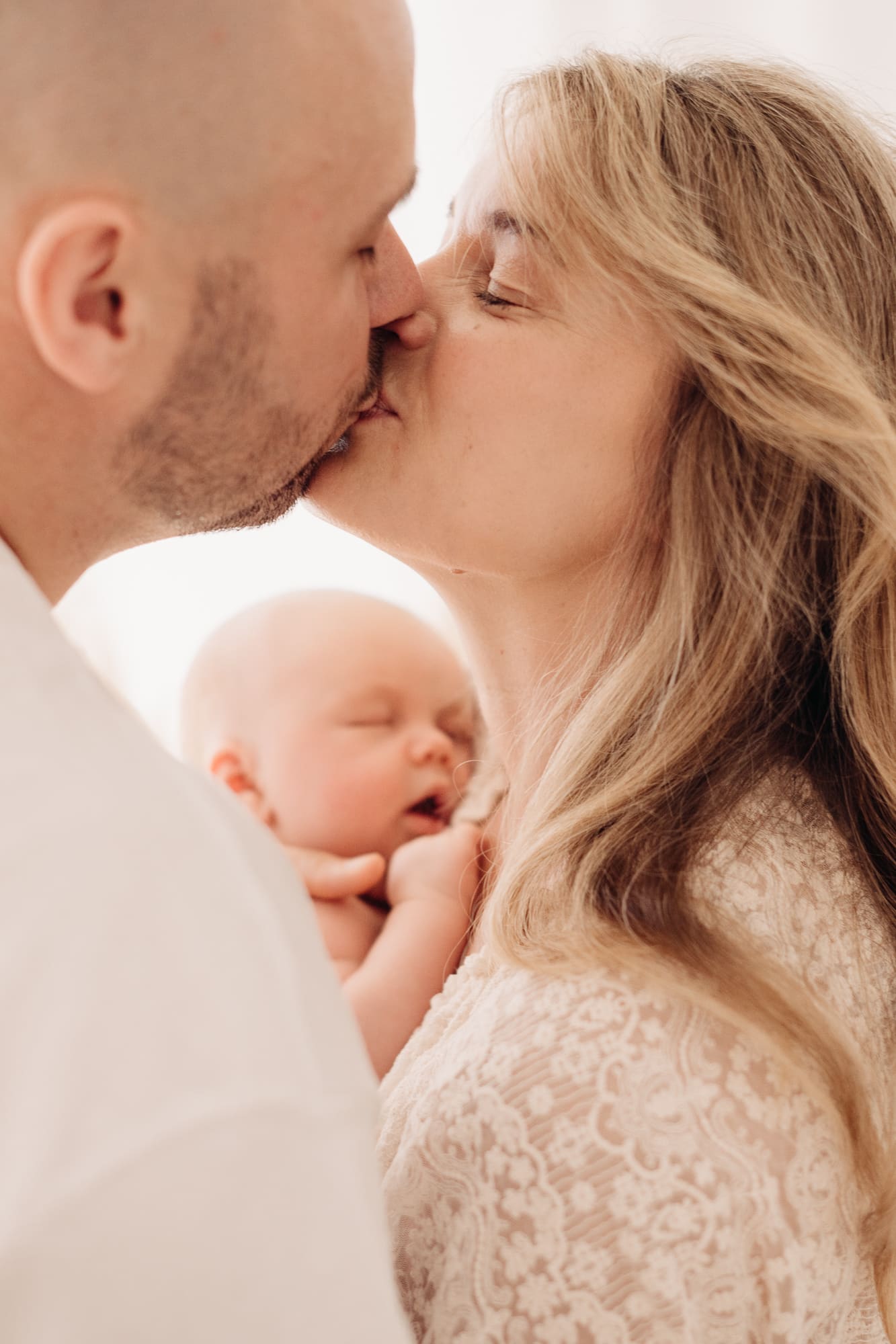 Eltern küssen sich liebevoll über ihrem schlafenden Neugeborenen — Newborn-Fotografie Bottrop