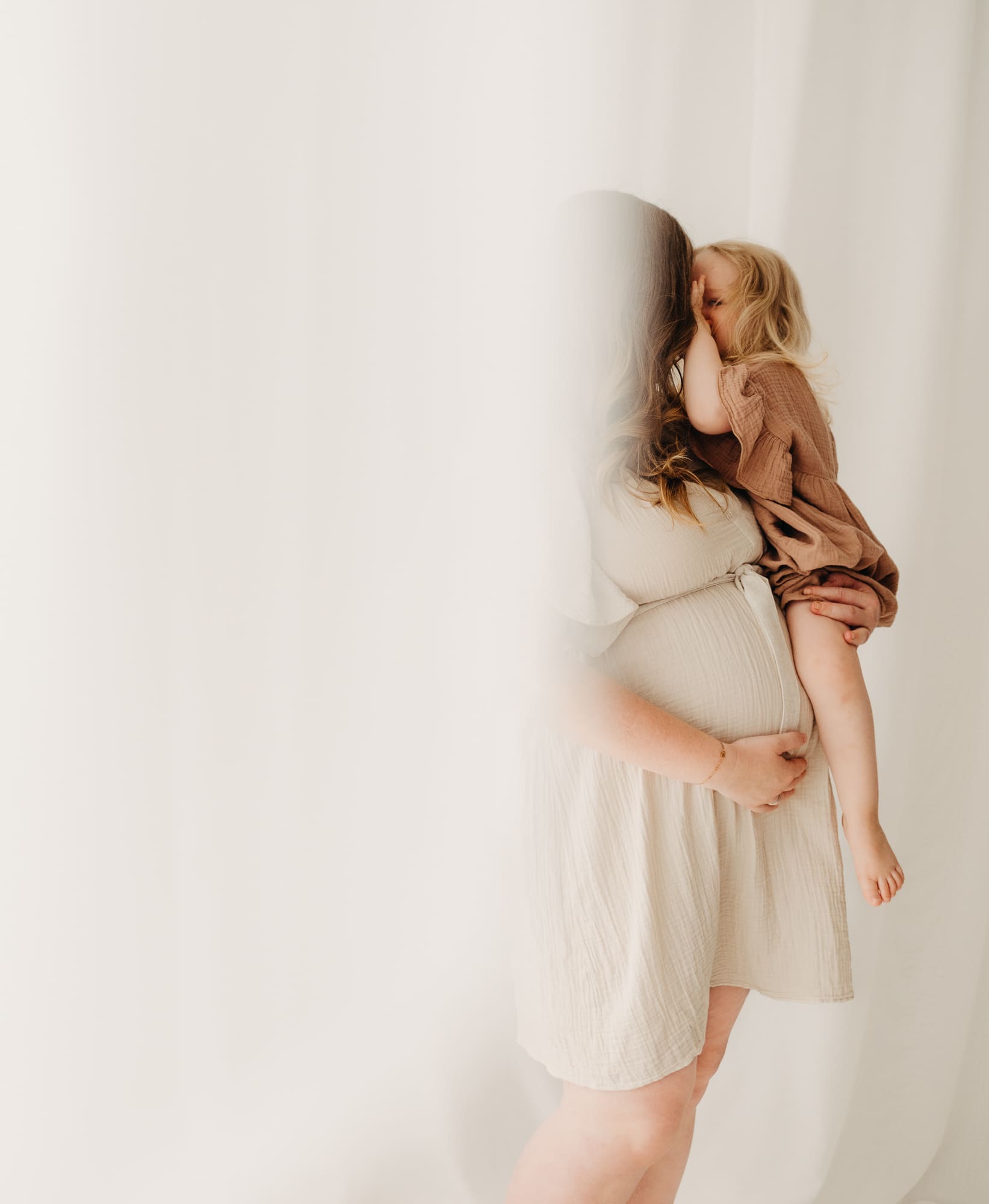 Schwangere Mama trägt ihr Kleinkind auf dem Arm, es küsst sie zärtlich ins Haar — Babybauch-Shooting Bottrop