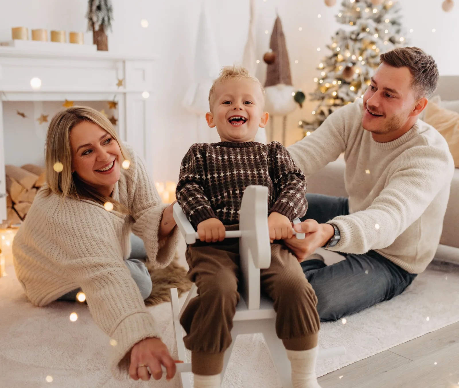 Lachendes Kind auf dem Schaukelpferd, Mama und Papa daneben, dahinter der beleuchtete Weihnachtsbaum — Weihnachts-Mini-Shooting bei Nicole Averkamp Fotografie in Bottrop