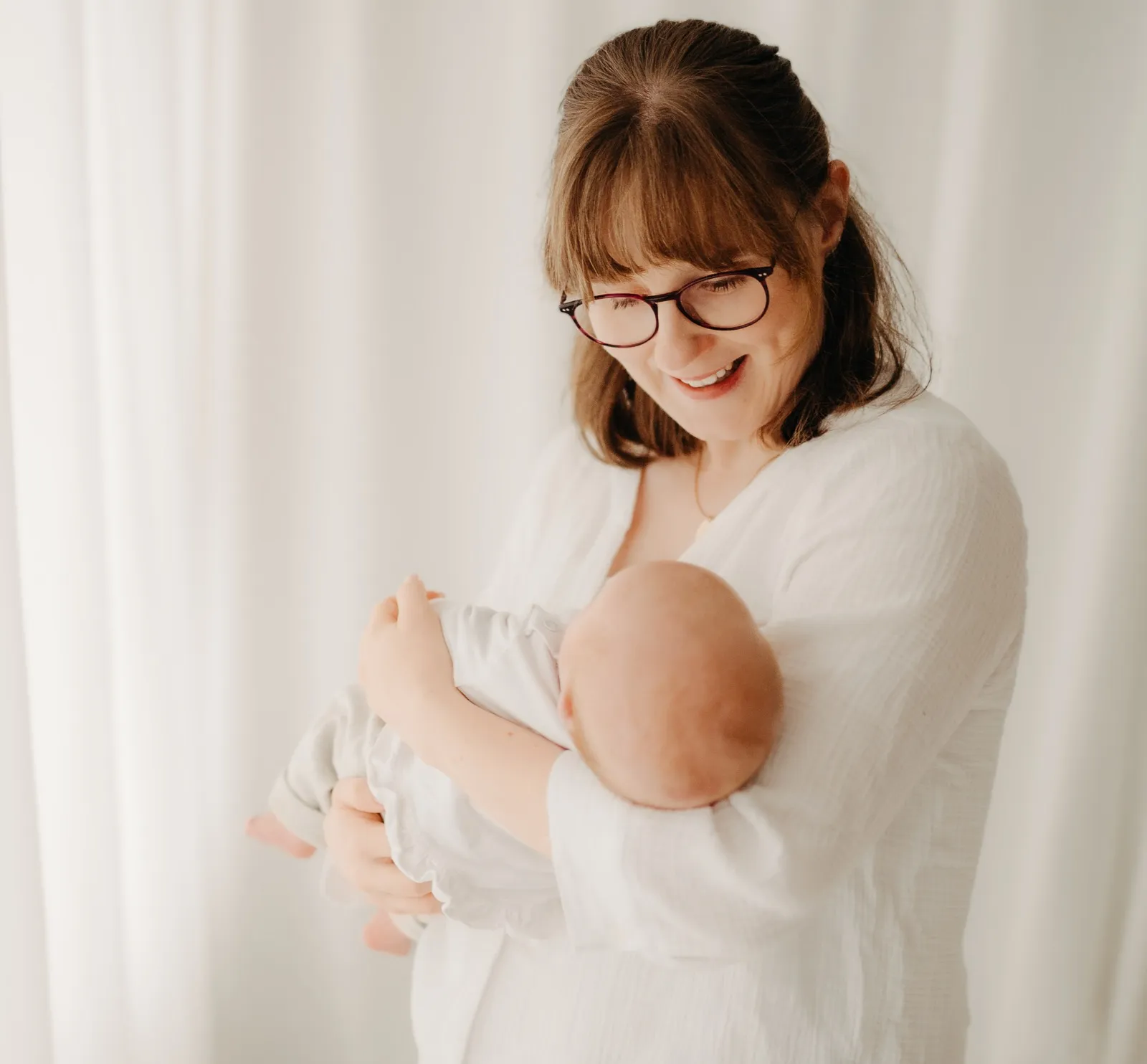 Mama hält ihr Baby im Arm und schaut lächelnd zu ihm hinunter